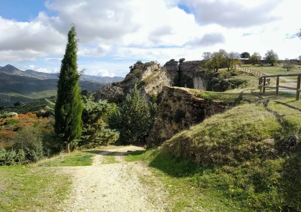 Camino de tierra entre cipreses y roca en el Sendero de los Zumaques